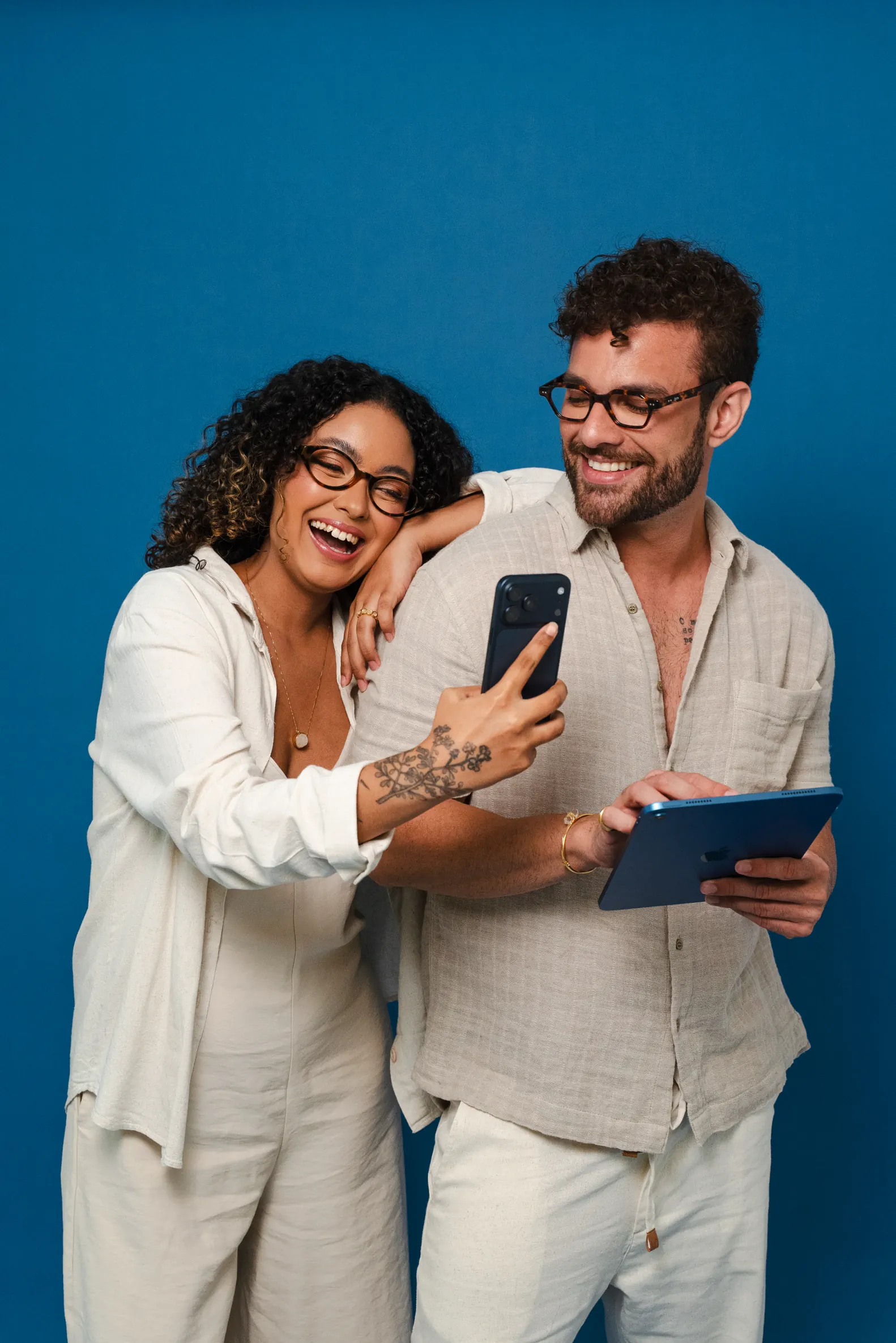 Uma mulher e um homem sorrindo, olhando juntos para um celular e um tablet
